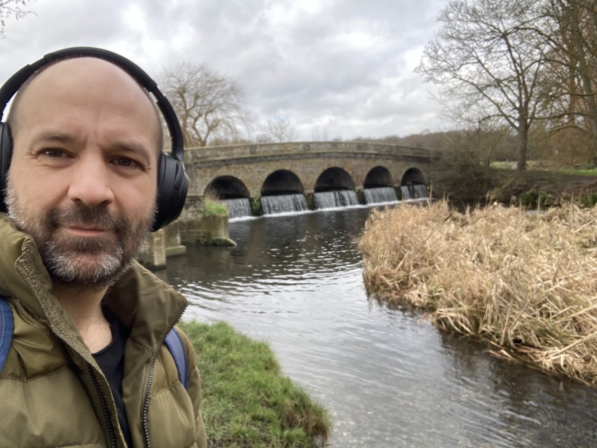 James Mason head and shoulders shot, pictured outdoors in front of a walking bridge and river